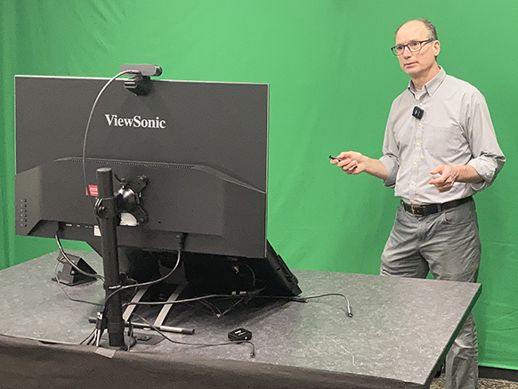 An instructor standing in front of a green screen in a video studio.